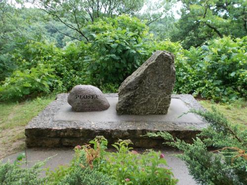 Two large stones on a concrete base, surrounded by lush greenery, with the word "PEOSTA" engraved on one stone.