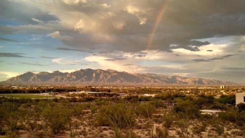 A scenic view of mountains under a cloudy sky, with a rainbow arching over a desert landscape.