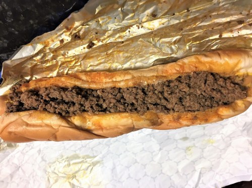 A sandwich filled with seasoned ground beef, served in a soft hoagie roll on crinkled paper.