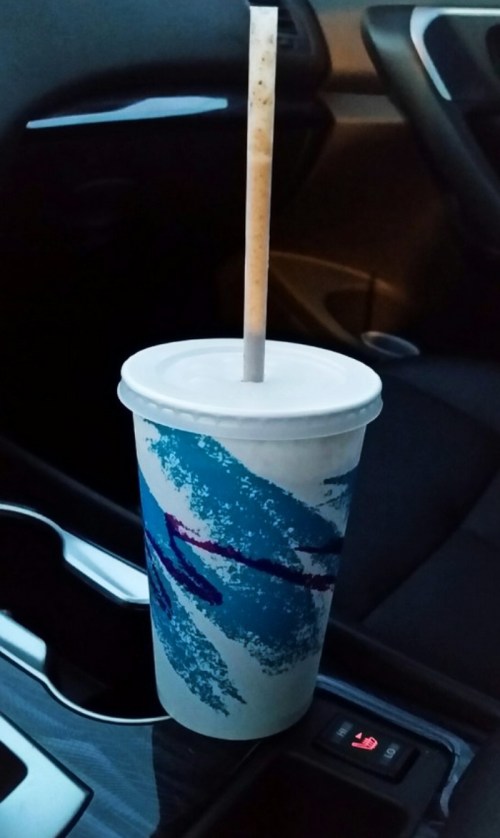 A disposable cup with a straw sits in a car's cup holder, featuring a blue and white abstract design.
