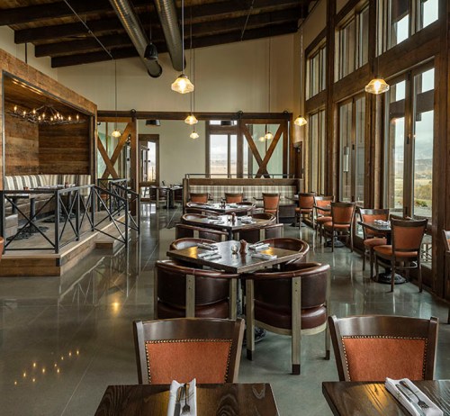 Modern restaurant interior with wooden accents, large windows, and round tables set for dining.