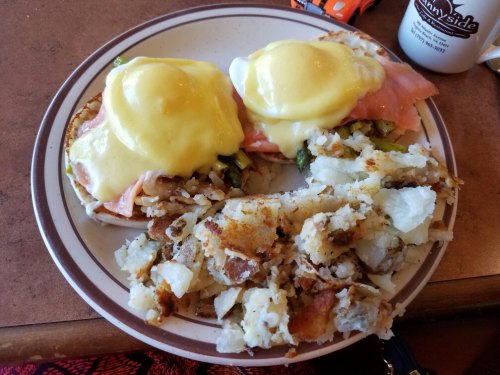 A plate with two eggs Benedict topped with hollandaise sauce and a side of crispy hash browns.