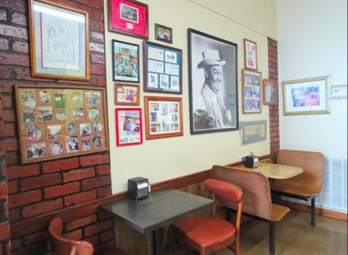 Cozy restaurant corner with wooden tables, chairs, and a wall adorned with framed photos and memorabilia.