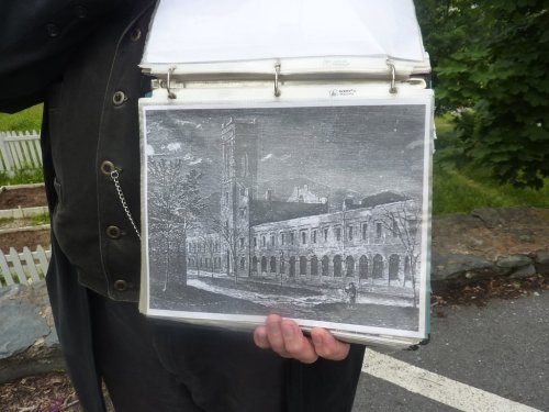 A person holds a binder open to a black-and-white illustration of a historic building with a tall clock tower.