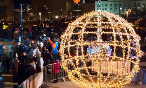 A large, illuminated globe made of lights hangs above a crowd at a festive outdoor event.