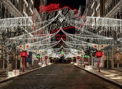 A festive street decorated with lights and holiday decorations, featuring a large "Netflix Here for the Holidays" sign.