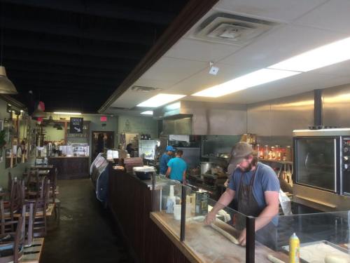 A busy restaurant kitchen with chefs preparing food, stainless steel appliances, and a counter with ingredients visible.