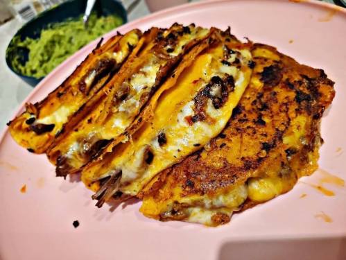 A plate of crispy, cheesy tacos filled with meat, served with a side of guacamole.
