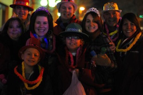 A group of people wearing festive hats and accessories, smiling together in a celebratory setting at night.