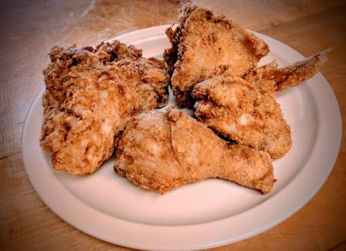 A plate of crispy fried chicken pieces, including drumsticks and wings, on a wooden surface.