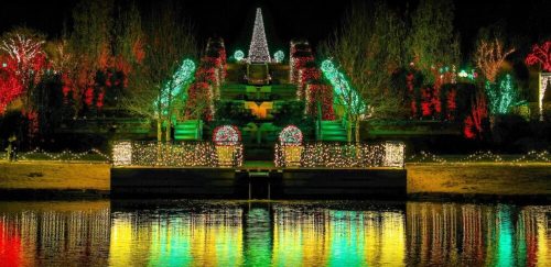 A beautifully lit park at night, featuring colorful holiday lights reflecting on a calm water surface.