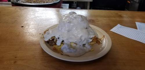 A plate of hearty breakfast featuring a mound of sausage gravy over eggs and crispy hash browns.