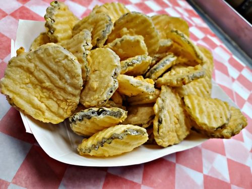 A serving of crispy, golden fried pickles in a paper tray on a red and white checkered tablecloth.