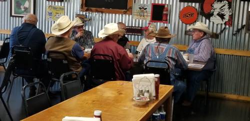 A group of men in cowboy hats sitting around a table in a rustic diner, engaged in conversation.