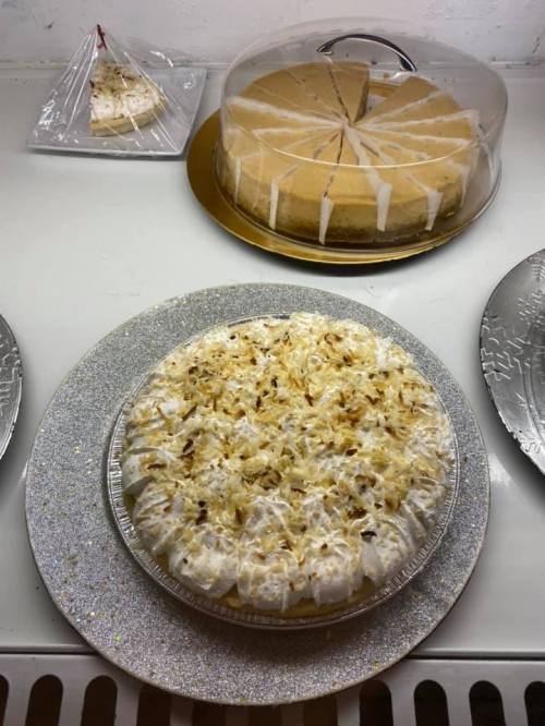 A table displaying two desserts: a coconut cream pie and a cheesecake under a dome, both on decorative plates.