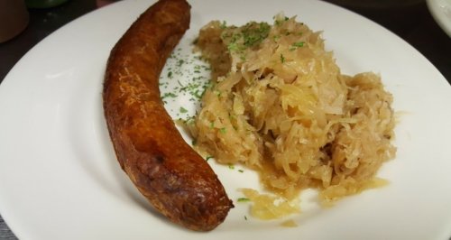 A plate featuring a golden-brown sausage alongside a serving of sauerkraut, garnished with parsley.