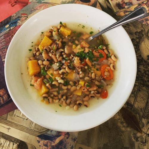 A bowl of black-eyed pea soup with vegetables, garnished with herbs, on a colorful patterned tablecloth.