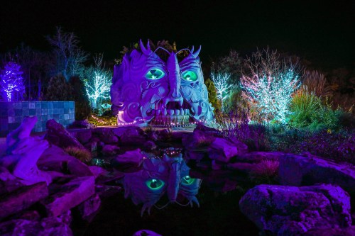 A large, illuminated sculpture of a face surrounded by colorful lights and a reflective pond at night.