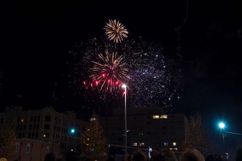 Colorful fireworks burst in the night sky above a cityscape, illuminating the dark with vibrant colors.