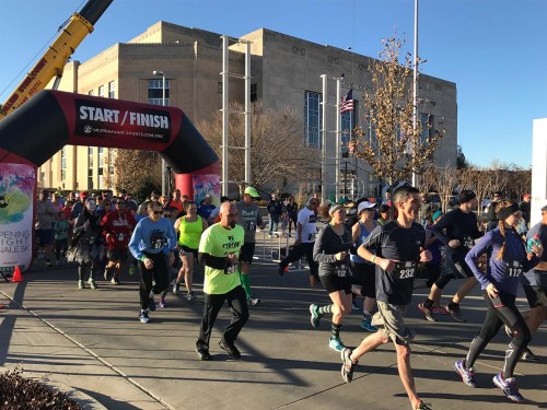 Runners start a race under a large "START/FINISH" arch, with a crowd and buildings in the background.