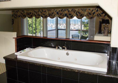 A spacious bathtub with a view of a marina through large windows, framed by decorative curtains.