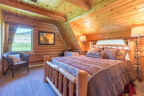 Cozy wooden bedroom with a log bed, patterned bedding, and a large window overlooking a scenic landscape.