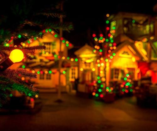 A festive scene with colorful lights adorning buildings and trees, creating a warm, holiday atmosphere at night.