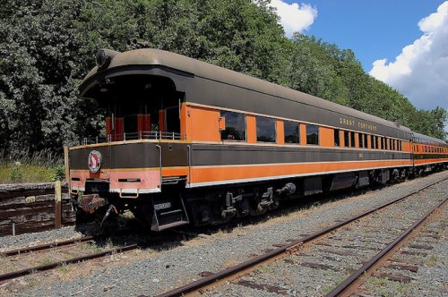 A vintage train car with orange and black stripes parked on a railway track surrounded by trees.