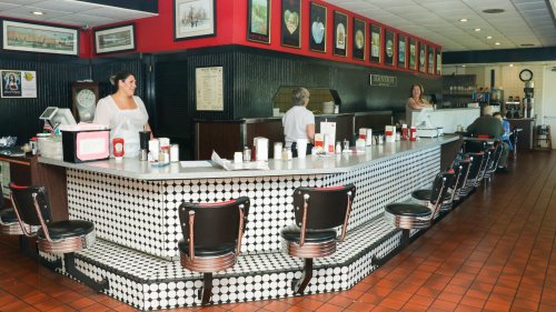 A retro diner interior with a black and white tiled counter, red walls, and staff serving customers.