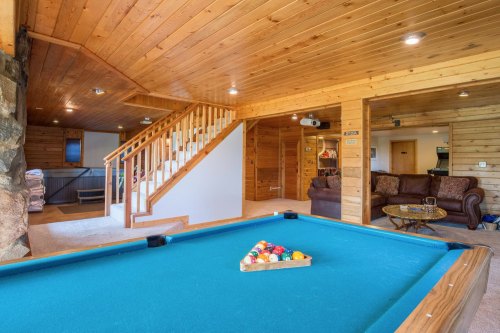 A cozy wooden interior featuring a pool table, staircase, and seating area with a couch and coffee table.