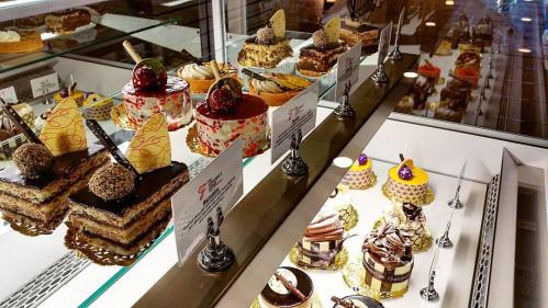 A display case filled with various colorful desserts, including cakes and pastries, each labeled with a name.