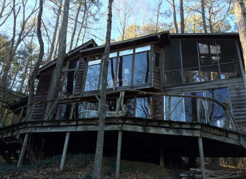A modern wooden cabin with large glass windows, nestled among trees on a hillside.