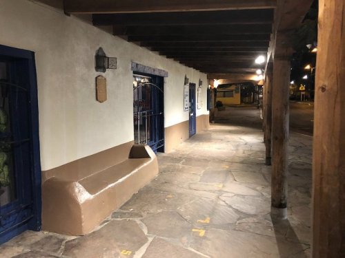 A quiet, dimly lit walkway with stone flooring and wooden beams, featuring a bench and blue accents on the walls.