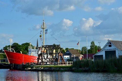 A red boat docked near a white building, with flags flying and a cloudy blue sky in the background.