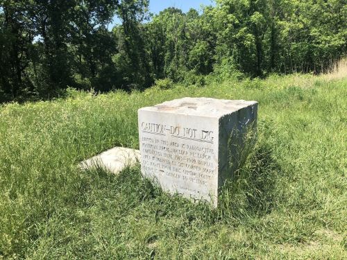 A large stone monument in a grassy area with a caution sign engraved on its side.