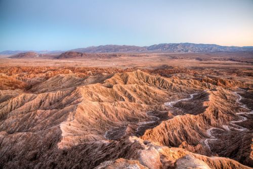 A panoramic view of rugged desert terrain with layered hills and mountains under a clear sky at dusk.