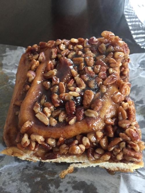 A close-up of a sticky pecan cinnamon roll topped with chopped pecans and a glossy caramel glaze.
