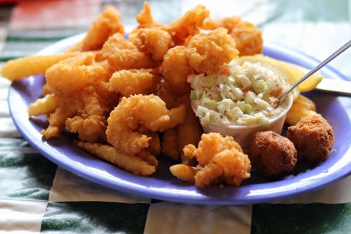 A plate of fried shrimp, French fries, coleslaw, and hushpuppies on a colorful tablecloth.