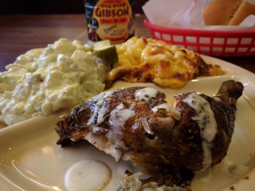 A plate featuring grilled chicken with sauce, macaroni and cheese, potato salad, and a drink in the background.