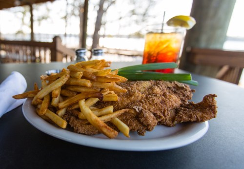 A plate of crispy fried fish with golden fries and a lemon wedge, accompanied by a glass of iced tea.