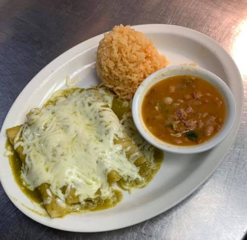 Plate of enchiladas topped with cheese, served with rice and a bowl of bean soup.