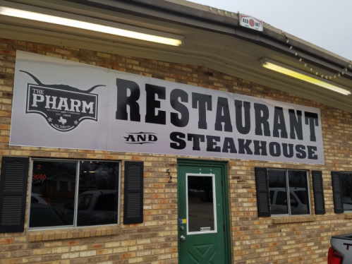 Sign for "The Pharm Restaurant and Steakhouse" on a brick building, featuring bold black lettering.