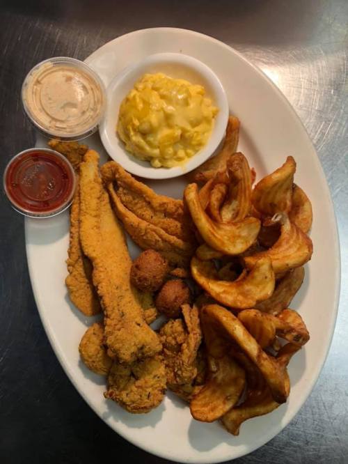 A platter featuring fried fish, chicken, macaroni and cheese, and potato wedges with dipping sauces.