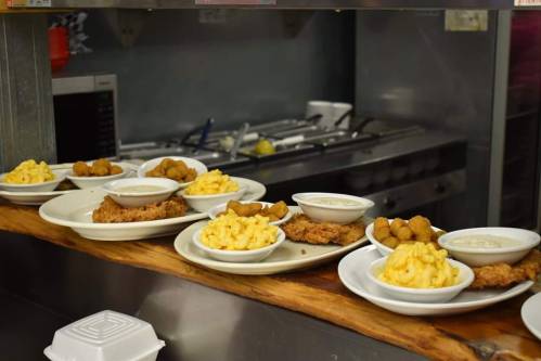 Plates of fried chicken, macaroni and cheese, and hushpuppies on a counter in a kitchen setting.
