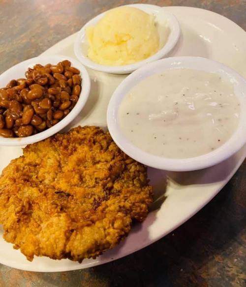 A plate featuring fried chicken, mashed potatoes, baked beans, and creamy gravy in small bowls.