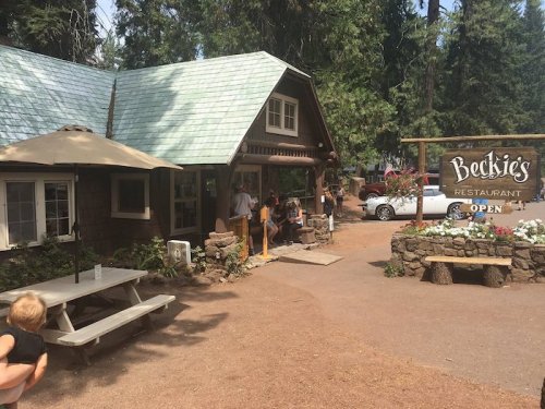 A cozy restaurant with a green roof, surrounded by trees, featuring a sign that says "Beckie's Restaurant - Open."