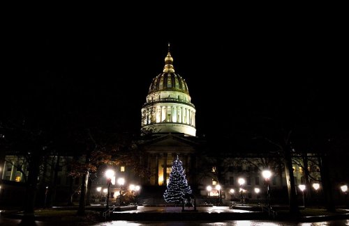 A lit Christmas tree stands in front of a grand dome building at night, surrounded by glowing street lamps.