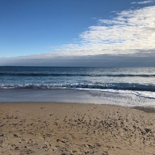 A serene beach scene with gentle waves lapping at the shore under a partly cloudy sky.