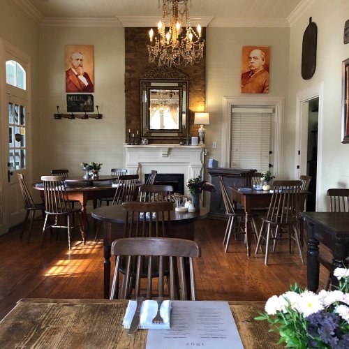Cozy dining room with wooden tables, chairs, and vintage decor, featuring a chandelier and portraits on the walls.