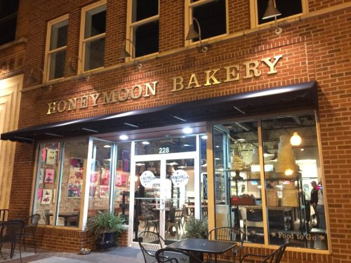 Exterior of Honeymoon Bakery at night, featuring a brick facade, large windows, and outdoor seating.